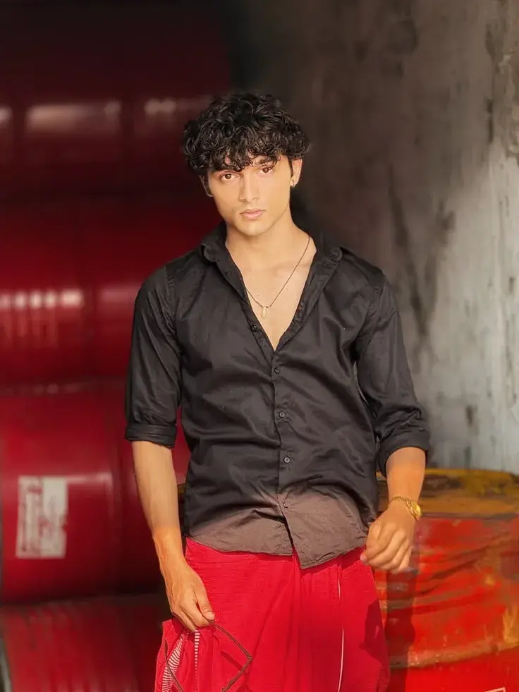 Candid Sunlit Industrial Warehouse Portrait Of Young South Asian Man In Black Button-Down Shirt And Red Dhoti