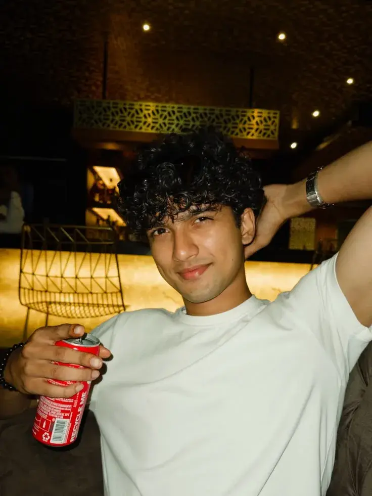 Candid Sunlit Lounge Bar Portrait Of Handsome Young South Asian Man With Curly Crop Hair Holding Red Soda Can
