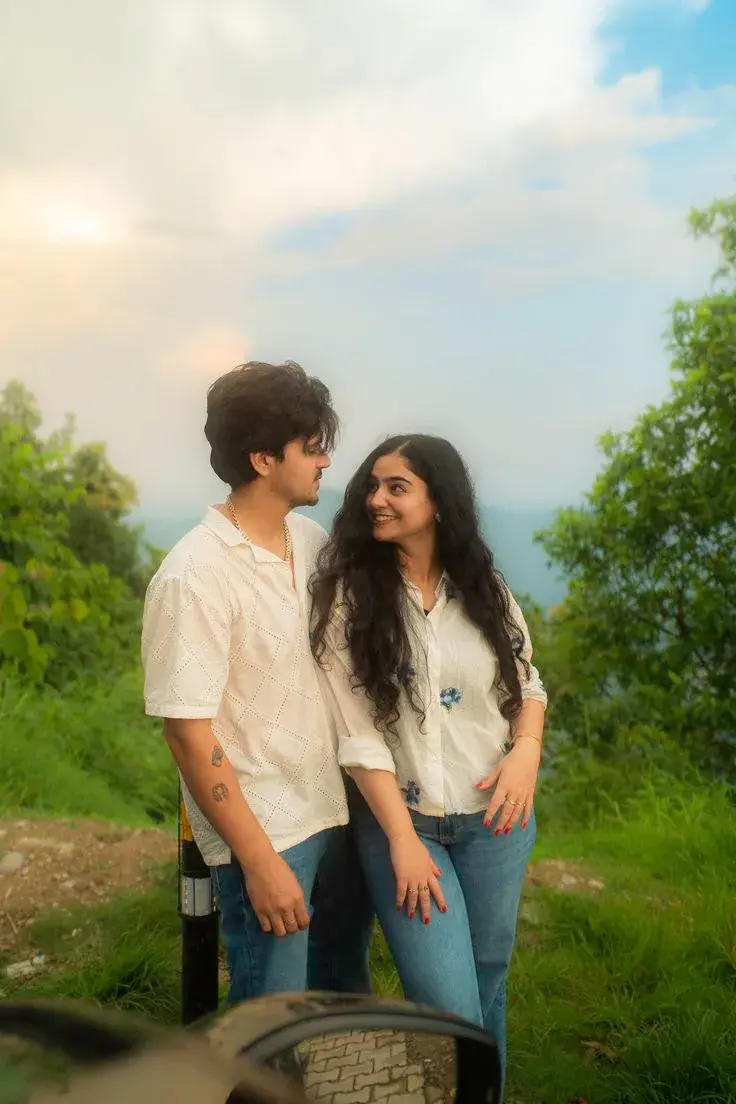 Candid Sunlit Mountain Overlook Portrait Of Affectionate Young South Asian Couple In White Resort Shirts And Denim