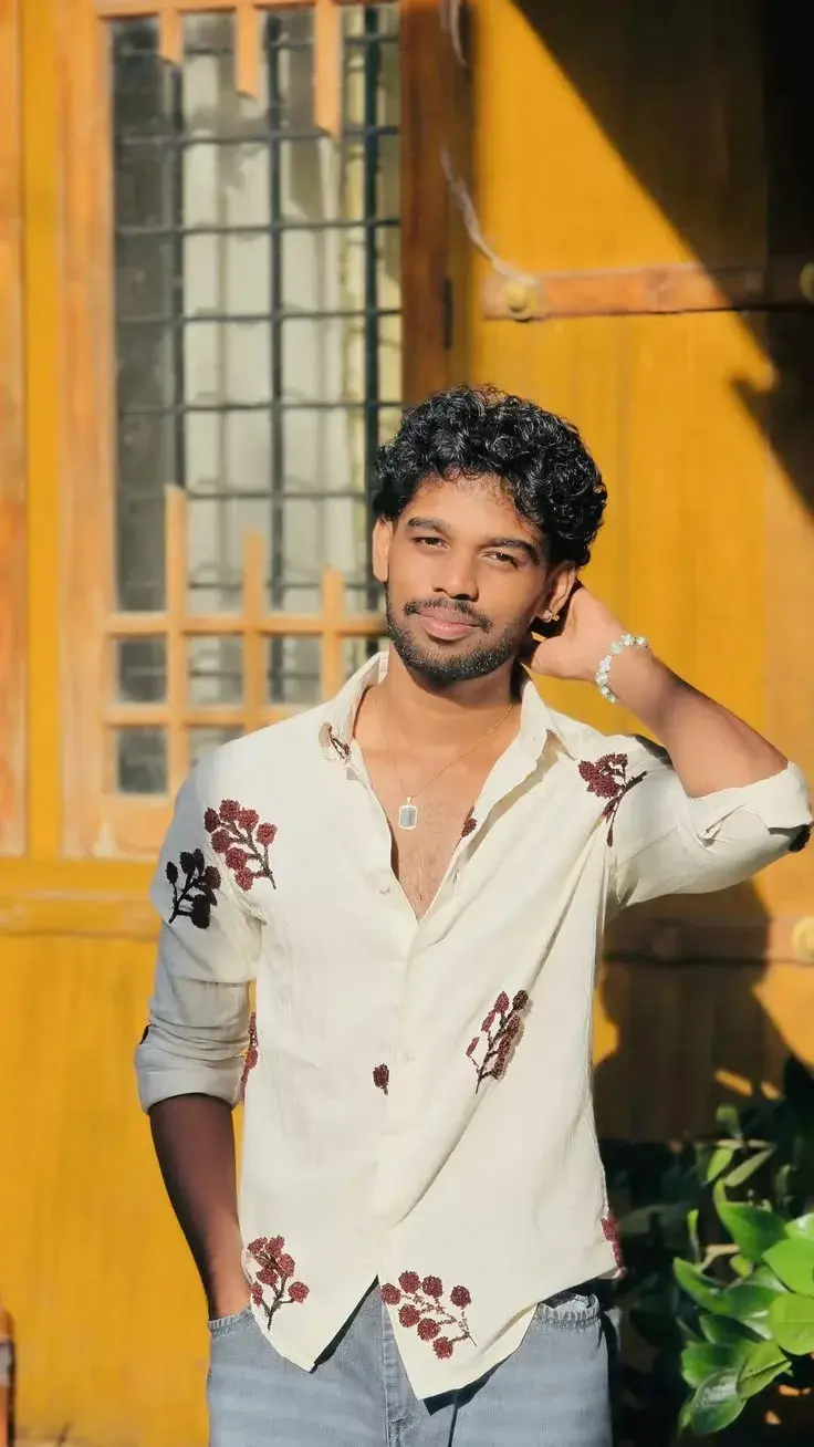 Candid Sunlit Outdoor Portrait Of Young South Asian Man With Curly Hair In Embroidered Cream Shirt Touching Neck