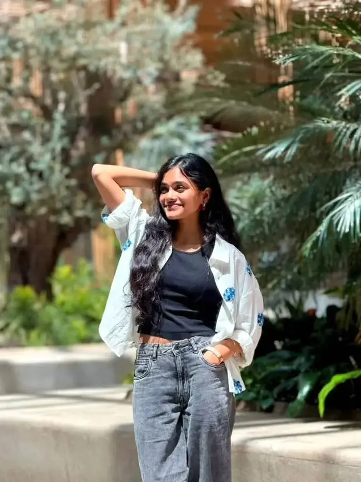 Candid Sunlit Resort Courtyard Portrait Of Smiling Young South Asian Woman With Long Wavy Hair In Embroidered White Over