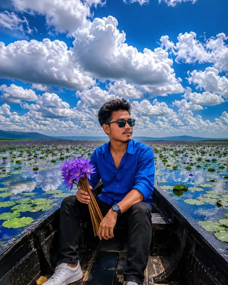 Candid Sunlit Wooden Boat Lake Portrait Of Handsome Young South Asian Man With Sunglasses Holding Purple Water Lilies