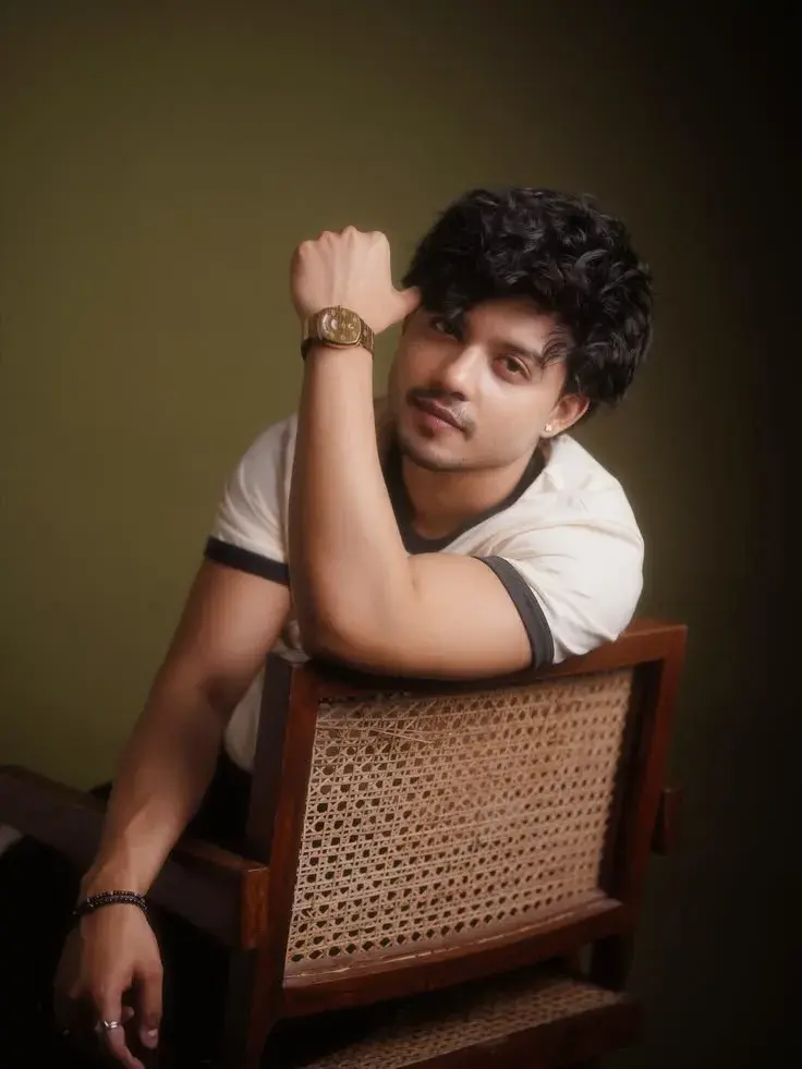 Candid Warm Studio Portrait Of Young South Asian Man Leaning On Cane Backrest Armchair With Hand On Watch