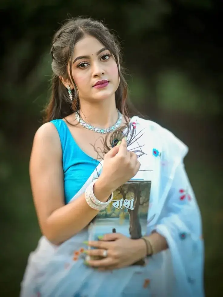 Candid Woman In Sky Blue Blouse And White Saree Holding Bengali Book And Peacock Feather