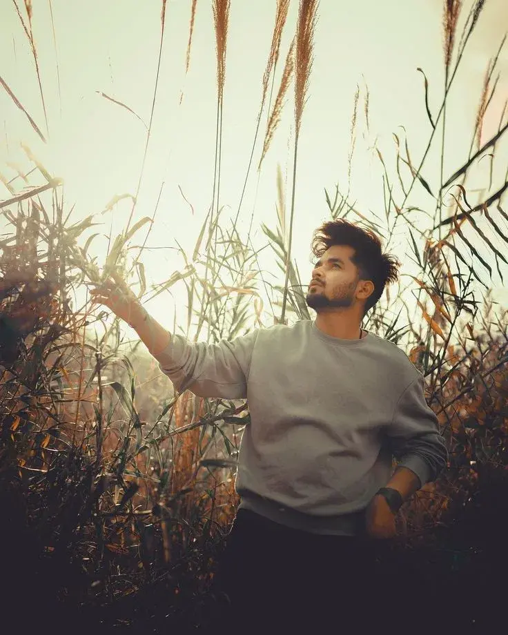 Candid Young Man In Grey Sweatshirt Standing Among Tall Reeds At Sunset