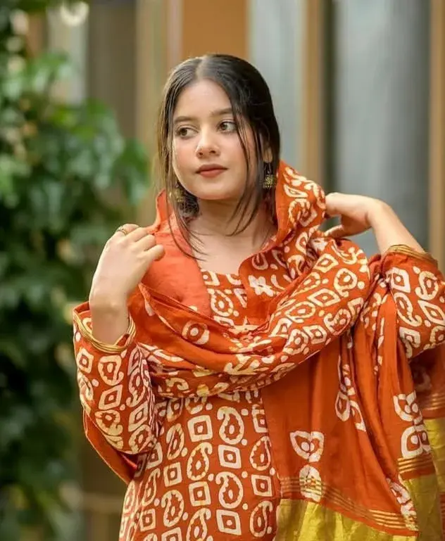 Candid Young Woman In Rust-Orange Batik Print Salwar Suit Adjusting Dupatta Outdoors
