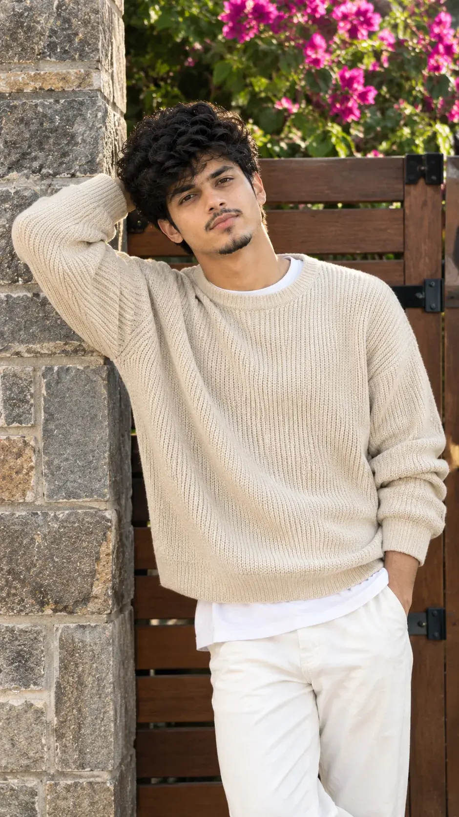 Elegant Young Man In Cream Knit Sweater Leaning Against A Stone Wall Outdoors