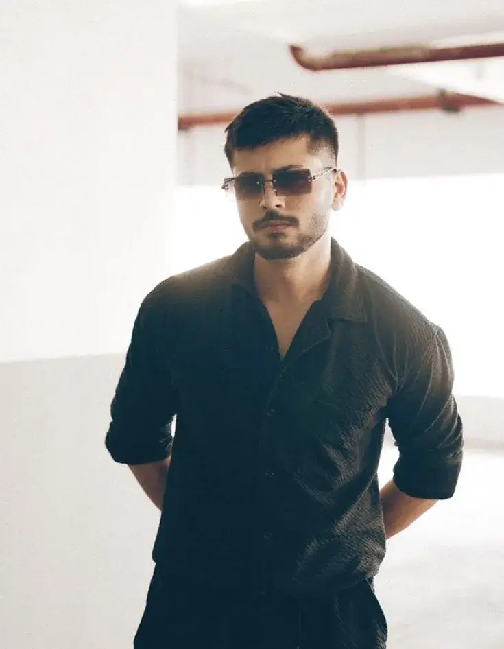 Moody Indoor Parking Garage Portrait Of Confident Young South Asian Man In Black Crinkled Shirt And Rimless Sunglasses