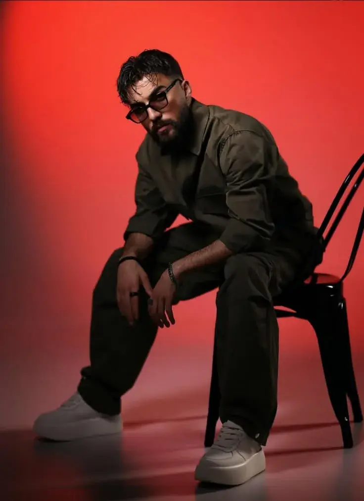 Moody Studio Full-Length Portrait Of Stylish Man Seated On Black Chair In Red Lighting