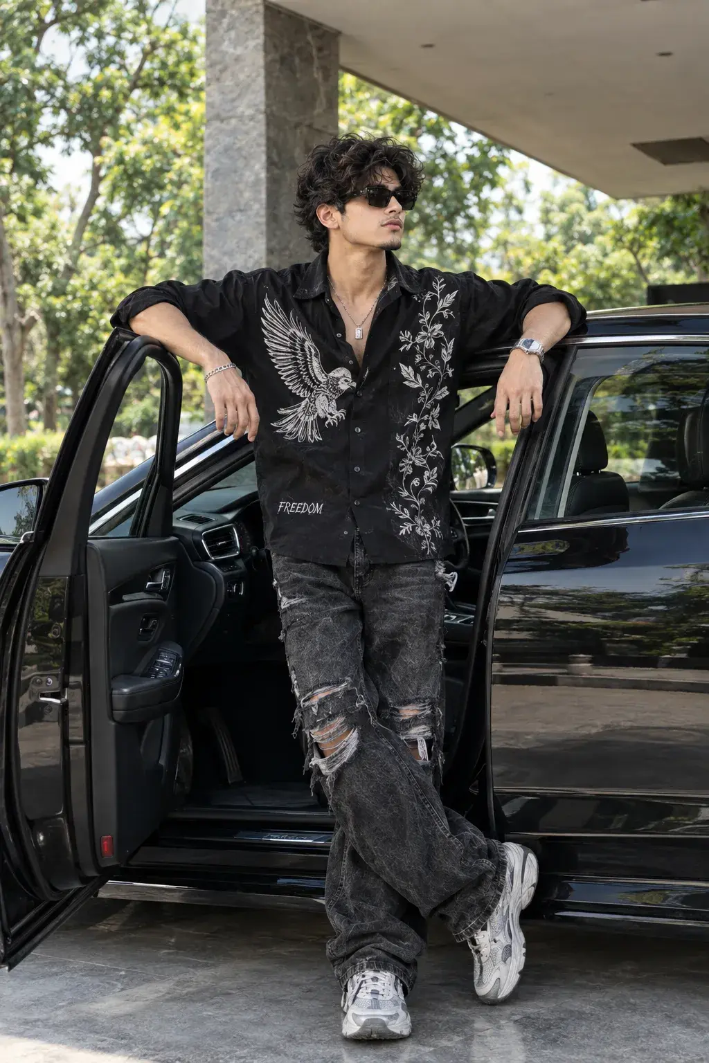 Stylish Young Man In Embroidered Black Shirt Leaning On Open Door Of Luxury Car