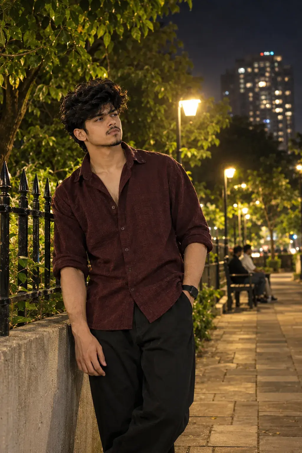 Thoughtful Young Man In Maroon Shirt Standing In An Urban Park At Night