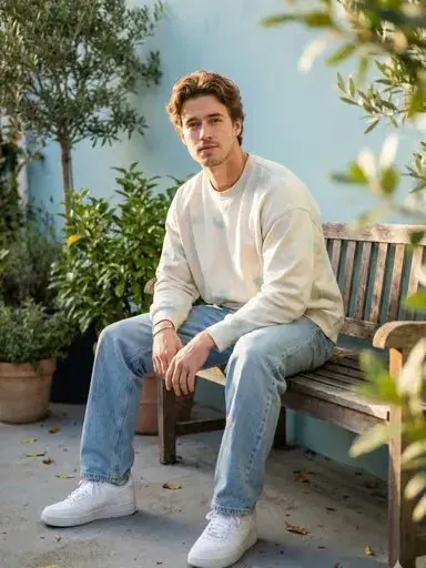 Young Man With Wavy Hair Sits Relaxed On A Small Rustic Wooden Bench